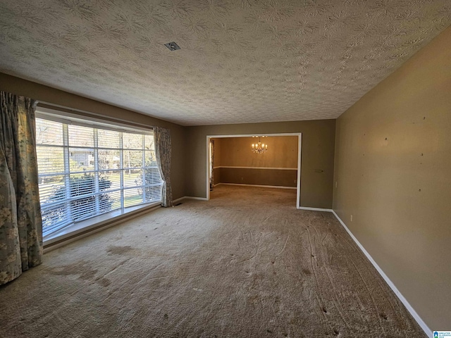 carpeted empty room with a textured ceiling, baseboards, and an inviting chandelier