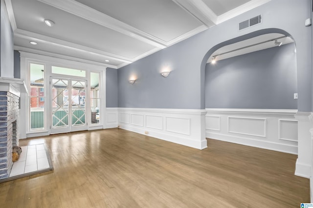 unfurnished room with visible vents, a brick fireplace, crown molding, beamed ceiling, and wood finished floors