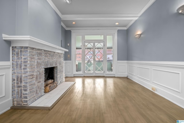 unfurnished living room featuring a wainscoted wall, ornamental molding, a fireplace, and wood finished floors