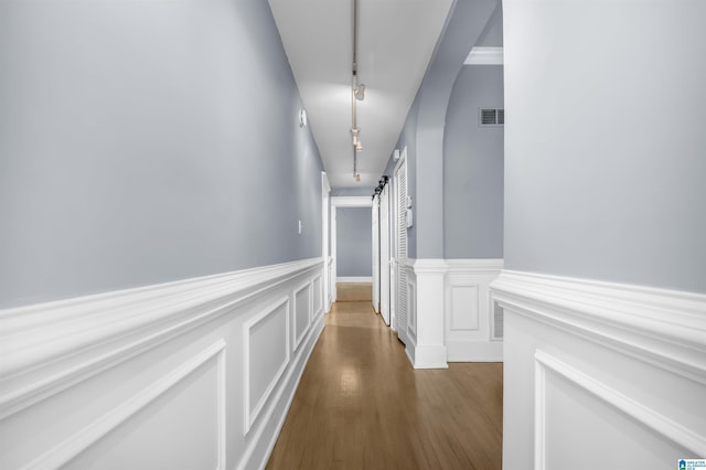 hall with visible vents, a wainscoted wall, dark wood-style floors, and track lighting