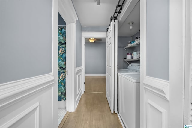 hall featuring light wood-type flooring, a barn door, a wainscoted wall, and washing machine and dryer