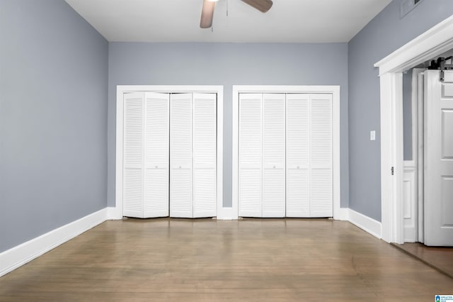 unfurnished bedroom with visible vents, wood finished floors, multiple closets, and baseboards