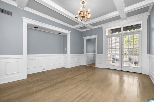 empty room featuring wood finished floors, visible vents, coffered ceiling, an inviting chandelier, and beamed ceiling