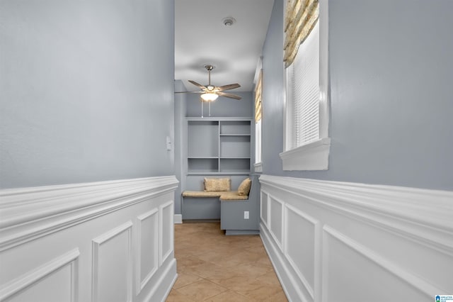 hall featuring light tile patterned floors, a decorative wall, and a wainscoted wall