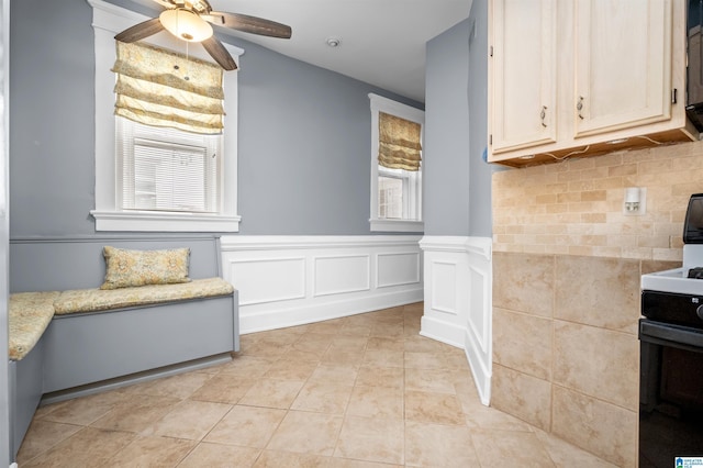 kitchen featuring a ceiling fan, light tile patterned flooring, wainscoting, range, and light stone countertops