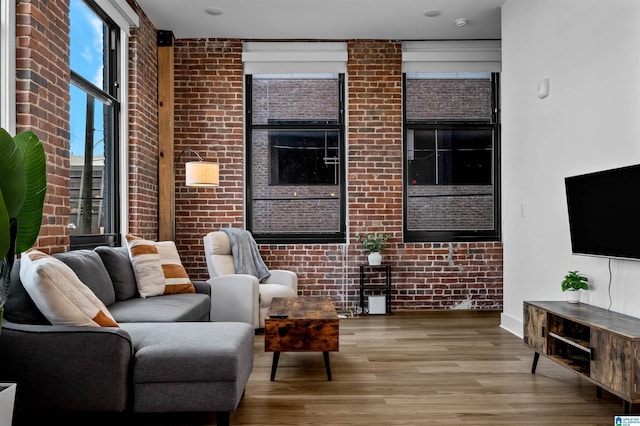 living area with brick wall and wood finished floors