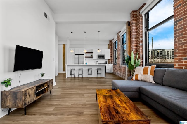 living area featuring light wood finished floors, visible vents, and brick wall