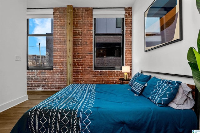 bedroom with brick wall, baseboards, and wood finished floors