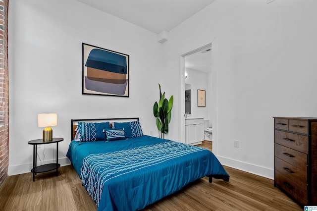 bedroom with connected bathroom, baseboards, and wood finished floors