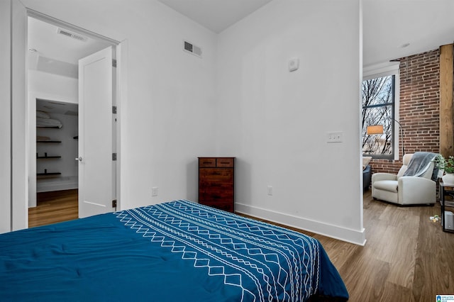 bedroom featuring visible vents, baseboards, wood finished floors, and brick wall