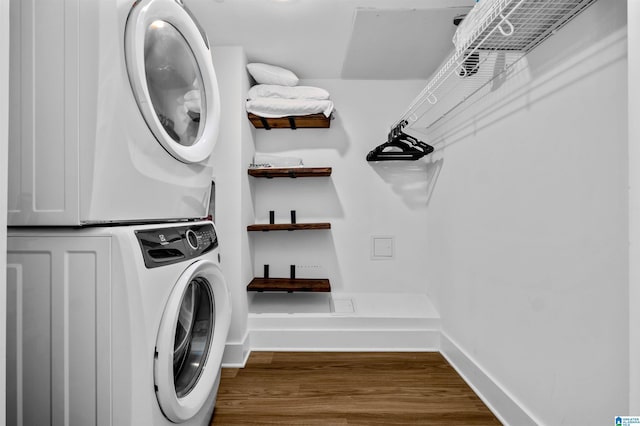 laundry area with laundry area, wood finished floors, baseboards, and stacked washer and dryer