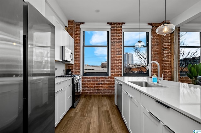 kitchen featuring brick wall, dark wood finished floors, a sink, light countertops, and appliances with stainless steel finishes