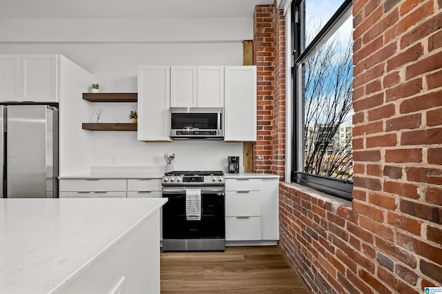 kitchen with open shelves, white cabinets, brick wall, and stainless steel appliances