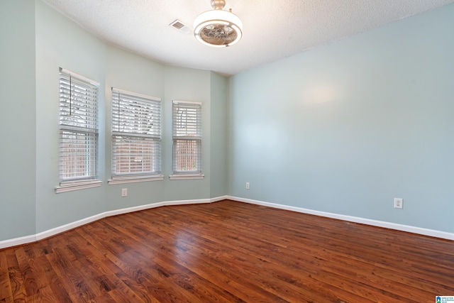 spare room featuring a textured ceiling, wood finished floors, visible vents, and baseboards