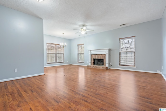 unfurnished living room featuring visible vents, ceiling fan with notable chandelier, wood finished floors, baseboards, and a brick fireplace