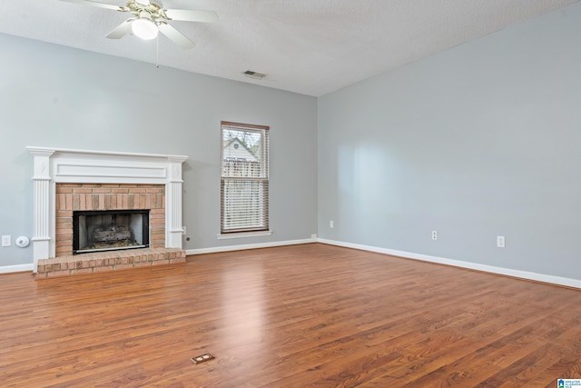 unfurnished living room with wood finished floors, visible vents, baseboards, a textured ceiling, and a brick fireplace