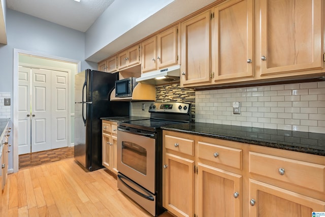 kitchen with dark stone counters, light wood-style floors, under cabinet range hood, appliances with stainless steel finishes, and backsplash