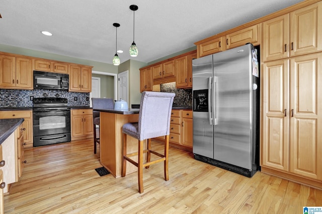 kitchen featuring dark countertops, light wood finished floors, black appliances, and a breakfast bar