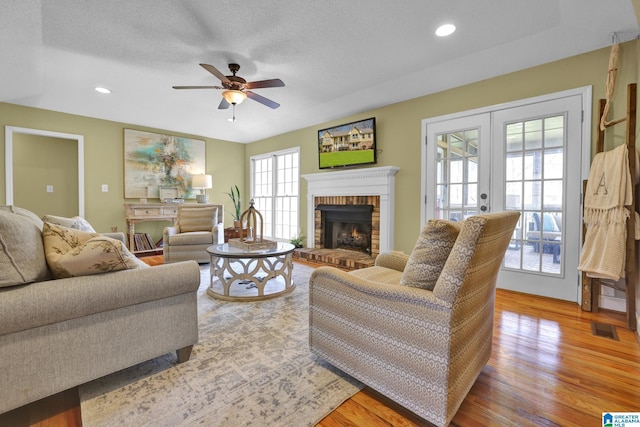 living room with visible vents, a brick fireplace, recessed lighting, light wood-style flooring, and french doors