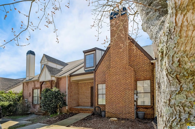 exterior space featuring a chimney, brick siding, and a shingled roof