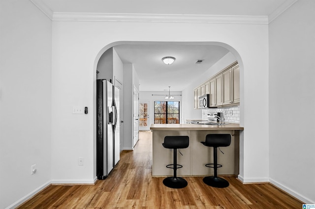 kitchen featuring decorative backsplash, light wood-type flooring, arched walkways, and stainless steel appliances