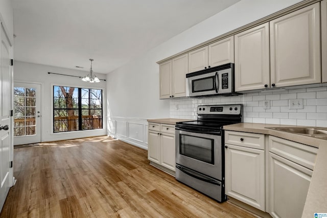 kitchen featuring light wood finished floors, decorative backsplash, wainscoting, appliances with stainless steel finishes, and a notable chandelier