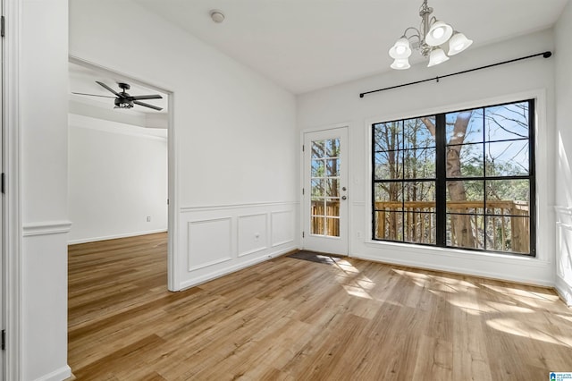 interior space with a decorative wall, wainscoting, ceiling fan with notable chandelier, and light wood-style floors