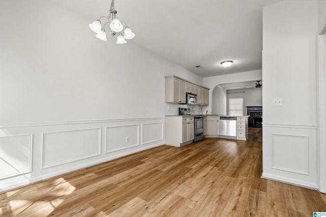 kitchen with light wood-type flooring, ceiling fan with notable chandelier, stainless steel appliances, light countertops, and hanging light fixtures