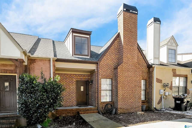 view of front of property featuring brick siding, a chimney, and a shingled roof