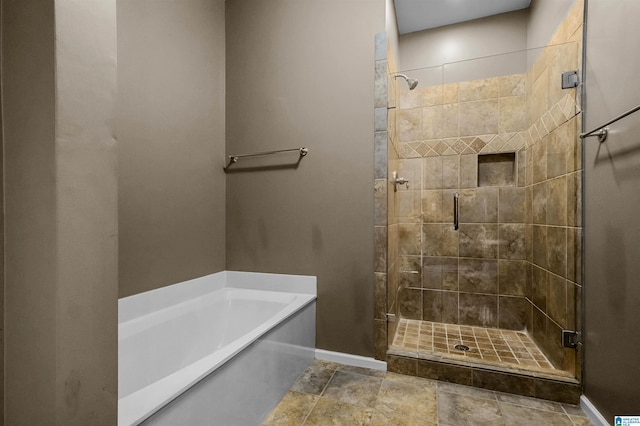 full bath with a bath, a shower stall, and baseboards