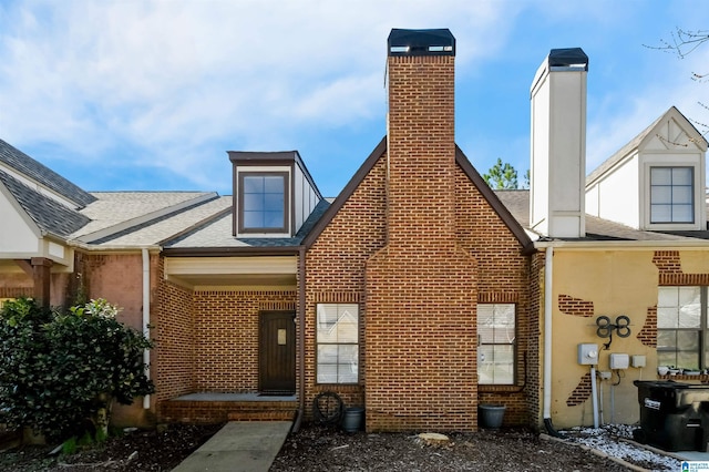 rear view of property featuring brick siding and roof with shingles