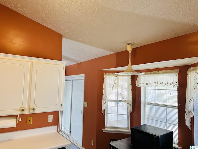 kitchen with a textured ceiling, white cabinetry, light countertops, and black microwave