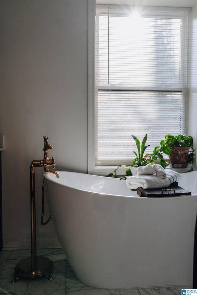 bathroom with a wealth of natural light, a freestanding tub, and marble finish floor