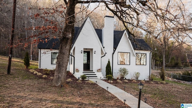 view of front facade with brick siding, a shingled roof, a chimney, and fence