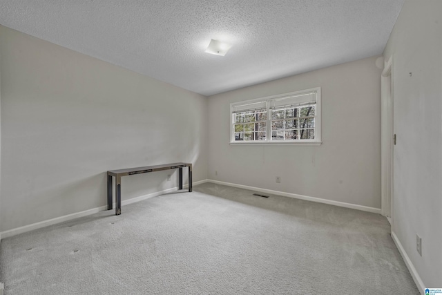 carpeted spare room with visible vents, baseboards, and a textured ceiling