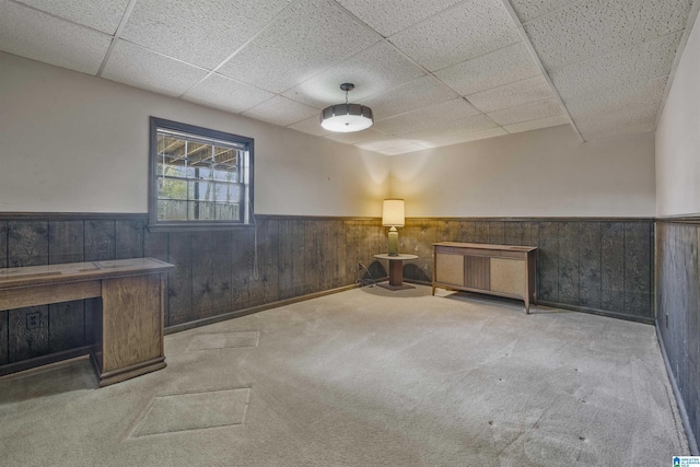 interior space featuring wooden walls, carpet, a drop ceiling, and wainscoting