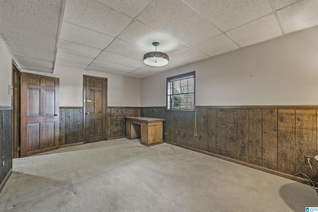 carpeted empty room featuring a drop ceiling, wood walls, and wainscoting