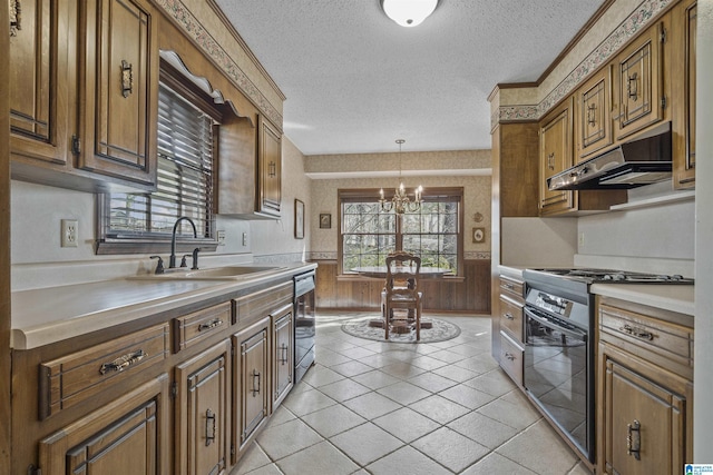 kitchen with a wainscoted wall, stainless steel gas stove, under cabinet range hood, a sink, and a textured ceiling