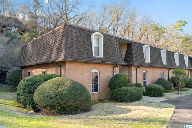 view of side of property with mansard roof, brick siding, and a shingled roof