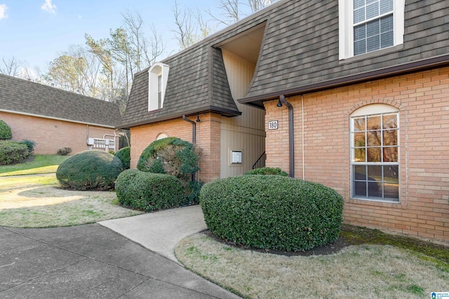 view of home's exterior featuring mansard roof, brick siding, and a shingled roof