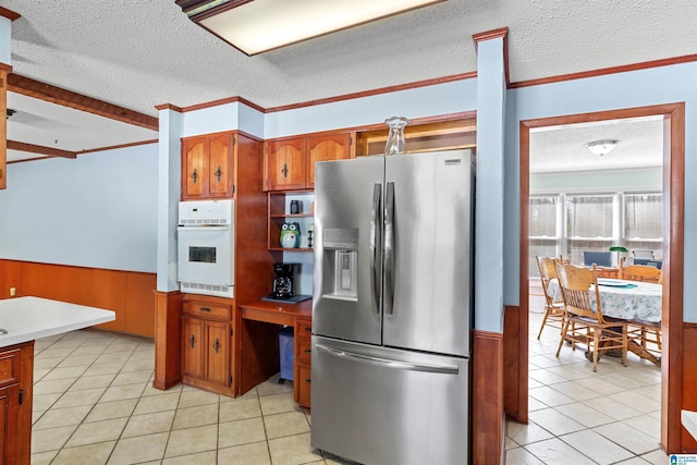 kitchen with oven, stainless steel fridge, wainscoting, brown cabinetry, and light tile patterned floors