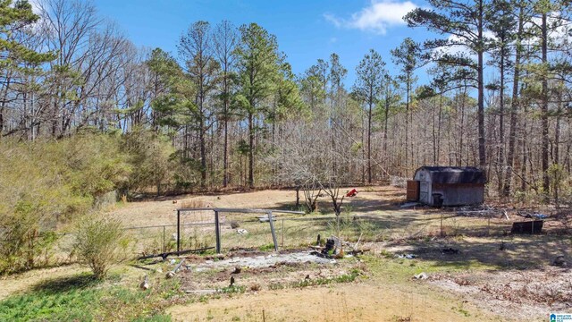 view of yard with a storage unit, fence, an outdoor structure, and a wooded view