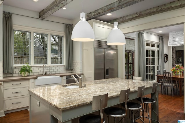 kitchen featuring beam ceiling, backsplash, built in fridge, and a sink