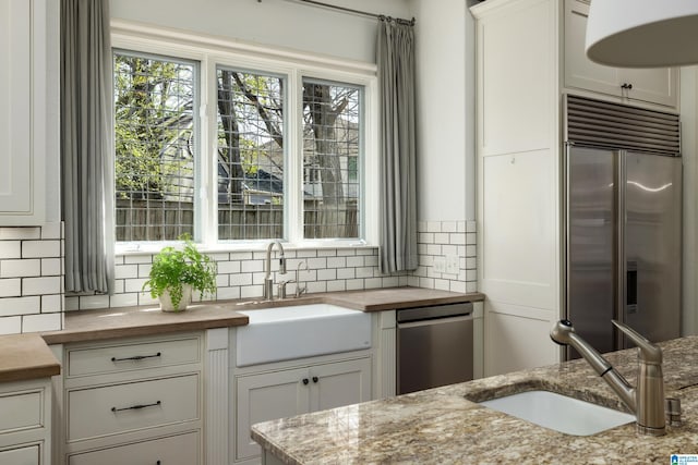 kitchen featuring backsplash, appliances with stainless steel finishes, wood counters, and a sink