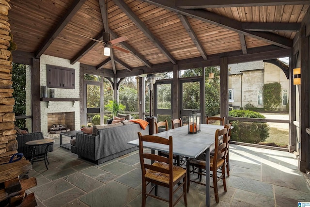 unfurnished sunroom with lofted ceiling with beams, an outdoor stone fireplace, wooden ceiling, and a ceiling fan