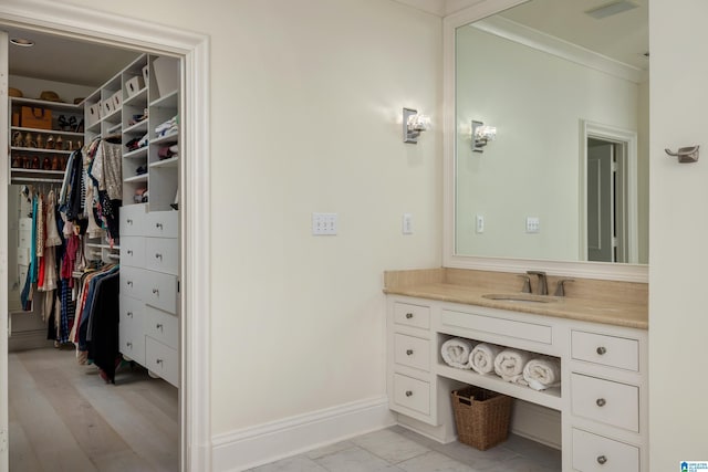 bathroom with a walk in closet, visible vents, crown molding, baseboards, and vanity