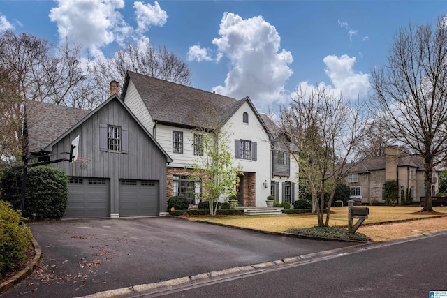 view of front of property with an attached garage, a shingled roof, a front lawn, a chimney, and driveway