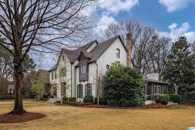 view of front of house with stucco siding, a chimney, a front lawn, and a sunroom