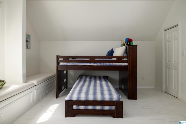 bedroom featuring baseboards, light wood-style floors, and vaulted ceiling