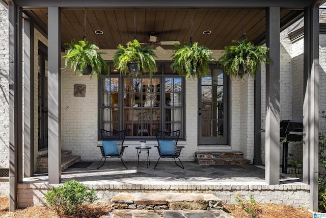 view of exterior entry with a porch, a ceiling fan, and brick siding